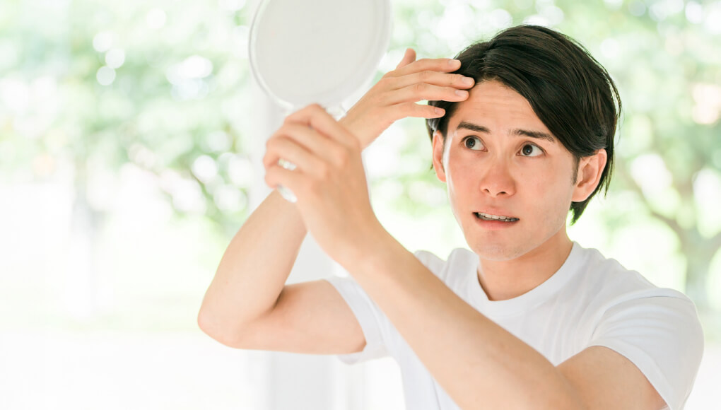 手鏡を見てAGA（生え際）を気にする男性