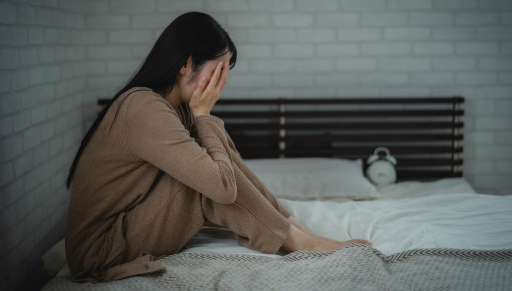 ベッドで顔を覆い悲しむ女性